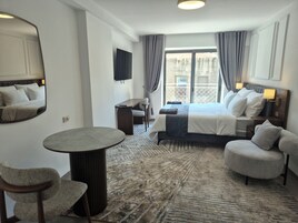 A hotel room with a bed, a desk, a chair, a round table, and a large mirror.
