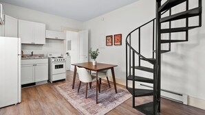 Une cuisine de taille réduite avec des meubles blancs, une table en bois et un escalier en colimaçon noir.