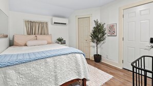 Une chambre à coucher avec un lit, une plante en pot, une porte et un climatiseur fixé au mur.