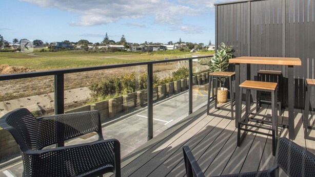 A deck with outdoor furniture, a view of a field, and a building in the background. - Warm and Welcoming on Wilson Road (Apartment #B3) (Waihi Beach)