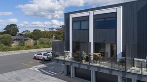A modern building with a flat roof, large windows, and a covered outdoor seating area. - Warm and Welcoming on Wilson Road (Apartment #B3) (Waihi Beach)