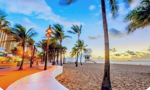 A beachside promenade with palm trees, a lifeguard tower, and a hotel in the background.