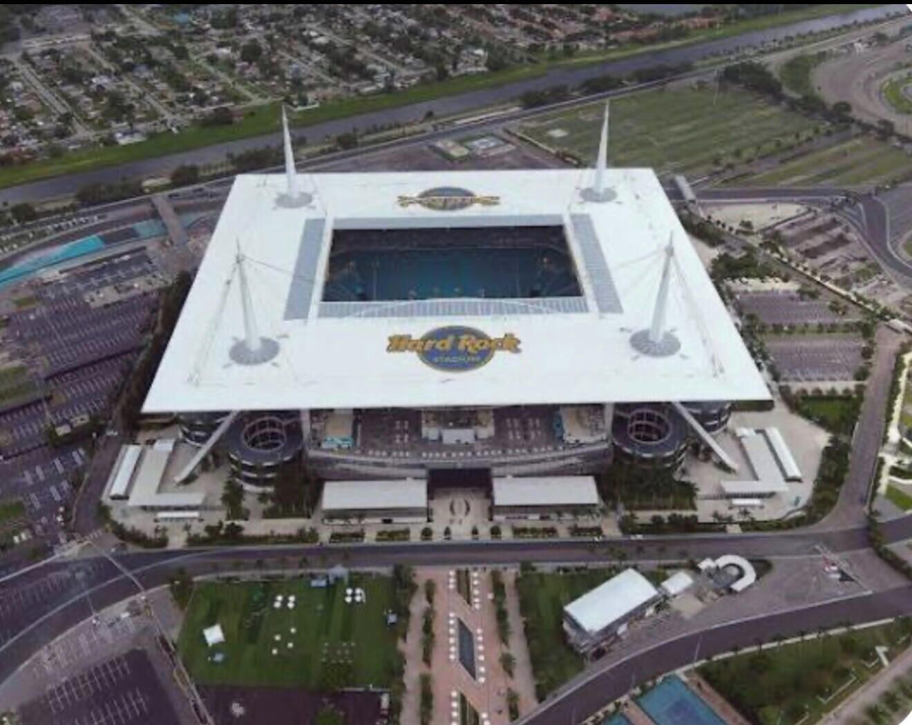Vista aerea di uno stadio con un logo centrale distintivo, circondato da aree di parcheggio e strade.