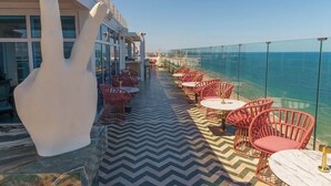 Une terrasse avec des sièges extérieurs, une grande sculpture blanche et une vue sur la mer.