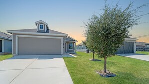 Un quartiere residenziale moderno con una casa a un piano, un garage, un prato curato e un piccolo albero.
