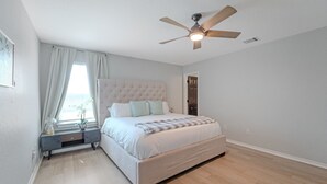 Una camera da letto con un letto grande, una ventola a soffitto, un comodino e una finestra con tende.