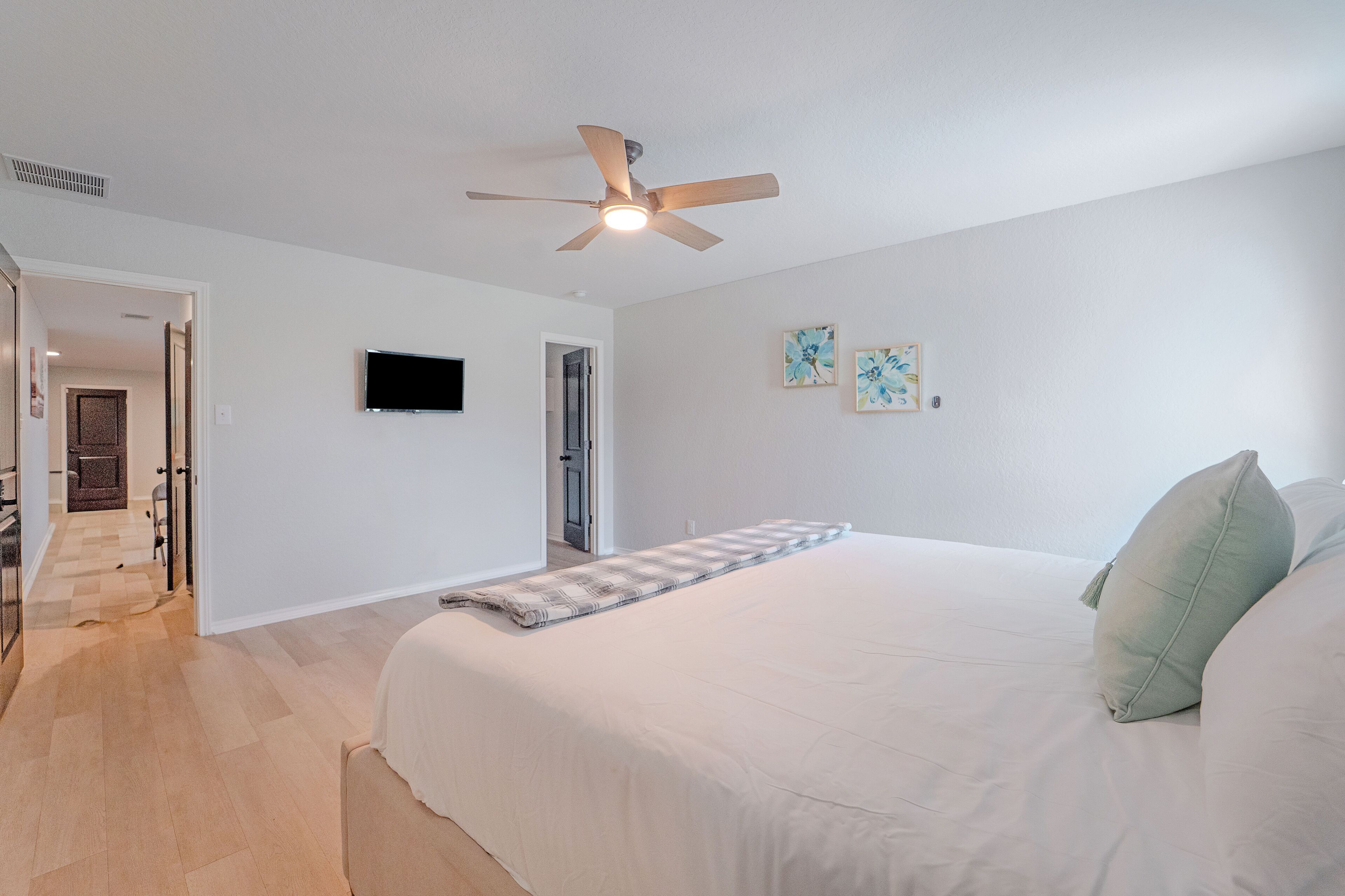 Une chambre à coucher avec un grand lit, un ventilateur de plafond et un téléviseur à écran plat fixé au mur.