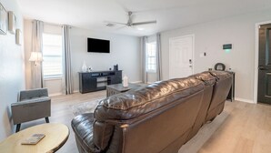 Un soggiorno con un divano in pelle, una TV a schermo piatto, una ventola a soffitto e un'area pranzo con tavolo e sedie.