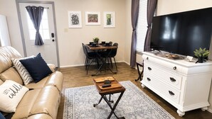 A living room with a sofa, a coffee table, a TV, a dining table with chairs, and a white dresser. - Hidden Gem Quiet 2BR Guest House Near Downtown with King Beds, Kitchen & Patio (Natchitoches)