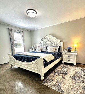 A bedroom with a large bed, a bedside table with a lamp, and a nightstand. - Hidden Gem Quiet 2BR Guest House Near Downtown with King Beds, Kitchen & Patio (Natchitoches)