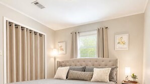 A bedroom with a large bed, a bedside table, a window with curtains, and a ceiling light. - Hidden Gem Quiet 2BR Guest House Near Downtown with King Beds, Kitchen & Patio (Natchitoches)