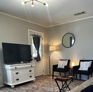 A room with a television on a dresser, a chair with a patterned pillow, a floor lamp, and a mirror on the wall. - Hidden Gem Quiet 2BR Guest House Near Downtown with King Beds, Kitchen & Patio (Natchitoches)