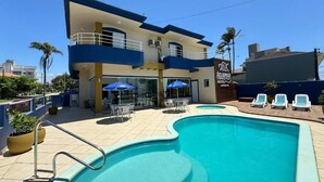 A hotel with a swimming pool, outdoor seating, and a clear blue sky. - Hotel Vila Águamar (Itapoá)