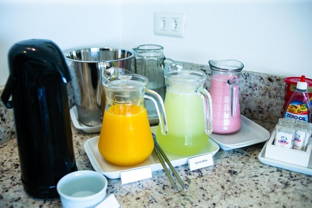 A kitchen counter with various glass containers holding different colored drinks, a black appliance, and a packet of sugar.
