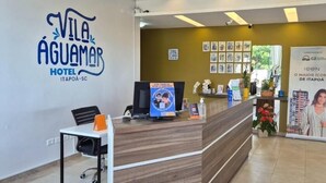 A hotel reception area with a wooden reception desk, a computer, and a signboard. - Hotel Vila Águamar (Itapoá)