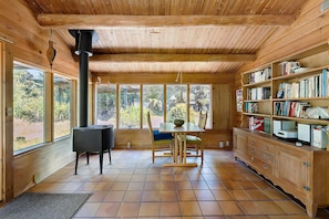 Un interior de madera con una mesa de comedor, sillas, una estantería y ventanas grandes.