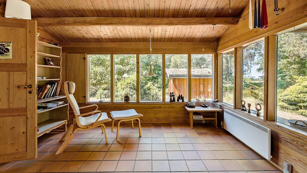 Een houten interieur met een groot raam, een stoel, een tafel en een radiator.