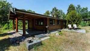 Een houten hut met een overdekte veranda, stenen trappen en twee ligstoelen.