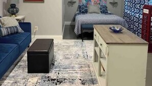 A compact bedroom with a bed, a blue sofa, a small table, and a nightstand. - Cottage Suite 3 in Fort Payne (Fort Payne)
