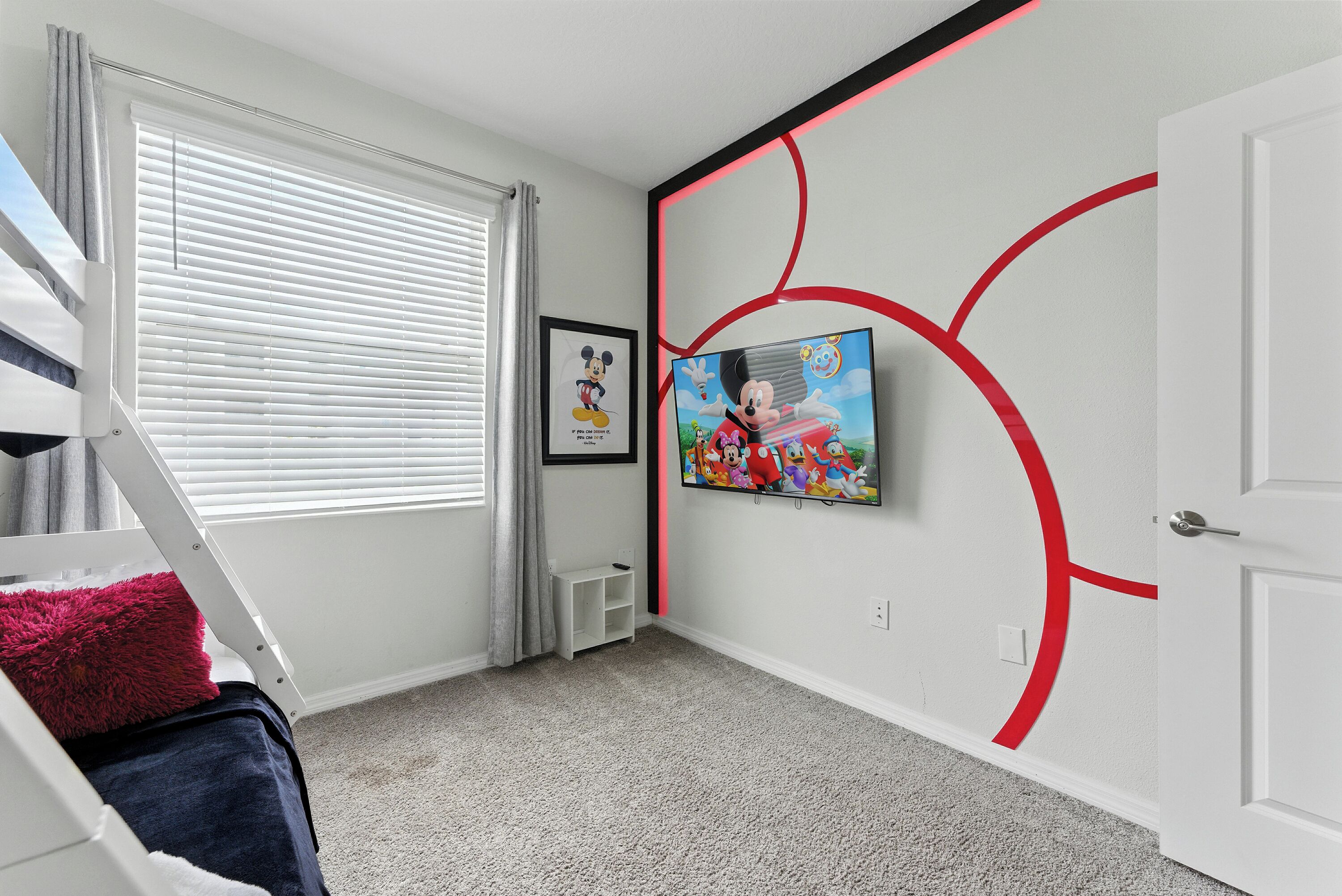 A room with a bunk bed, a framed picture, a television, and a door with a red accent.