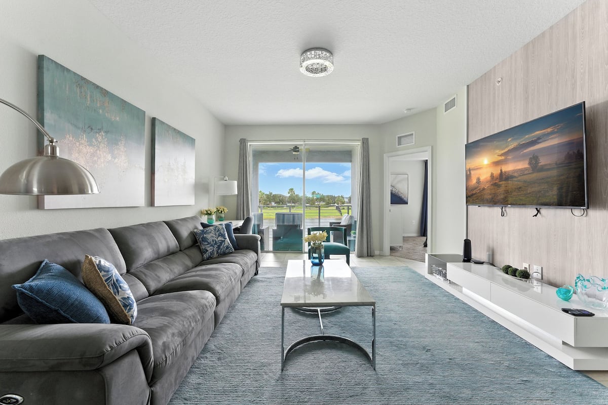 A modern living room with a grey sofa, a coffee table, and a TV on a wooden wall.