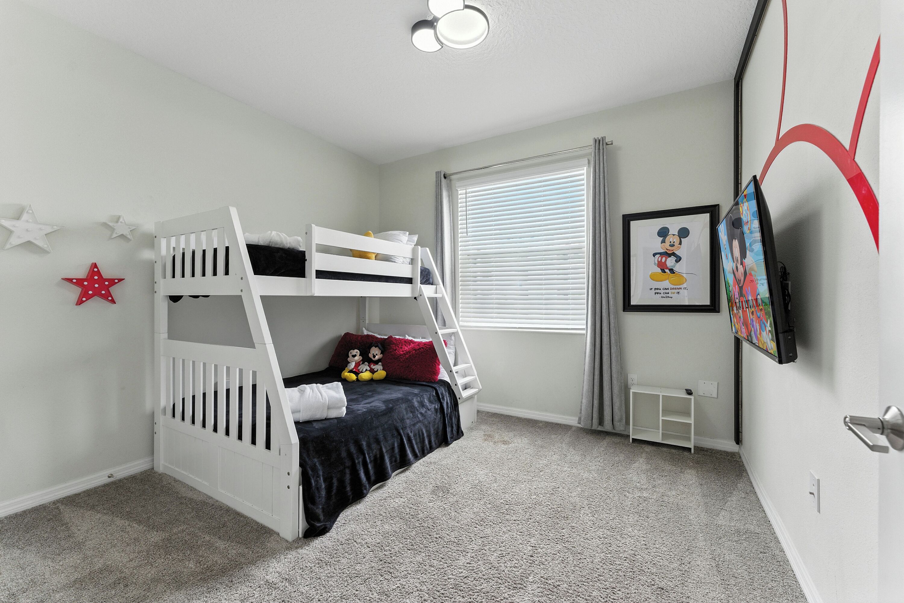 A child's bunk bed with a ladder, a small white shelf, and a framed picture on the wall.