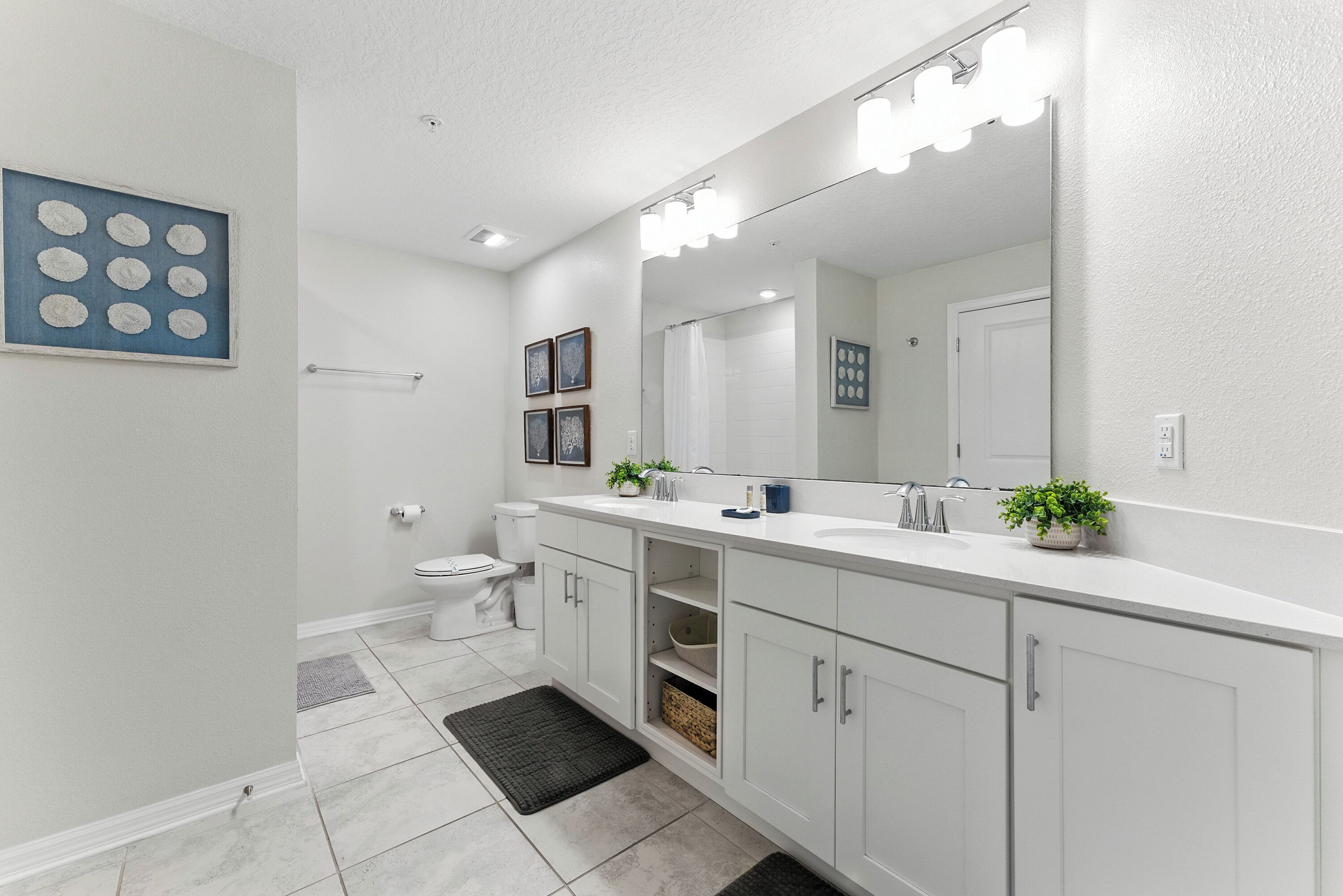 A modern bathroom with white cabinetry, a large mirror with lights, a toilet, and a shower area.