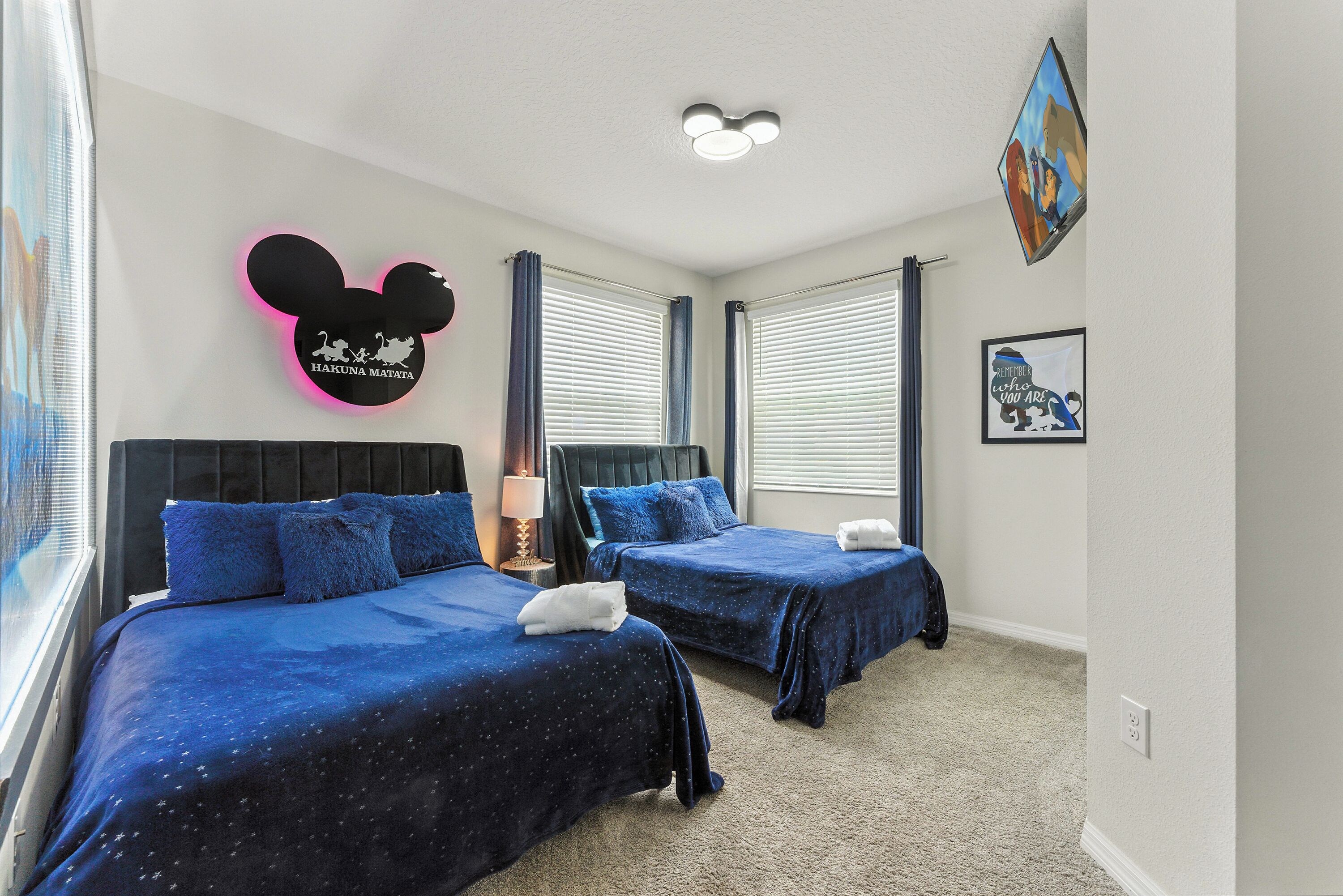 Ein Hotelzimmer mit zwei Betten, einer Wanddekoration mit Mickey Mouse und einem gerahmten Bild an der Wand.