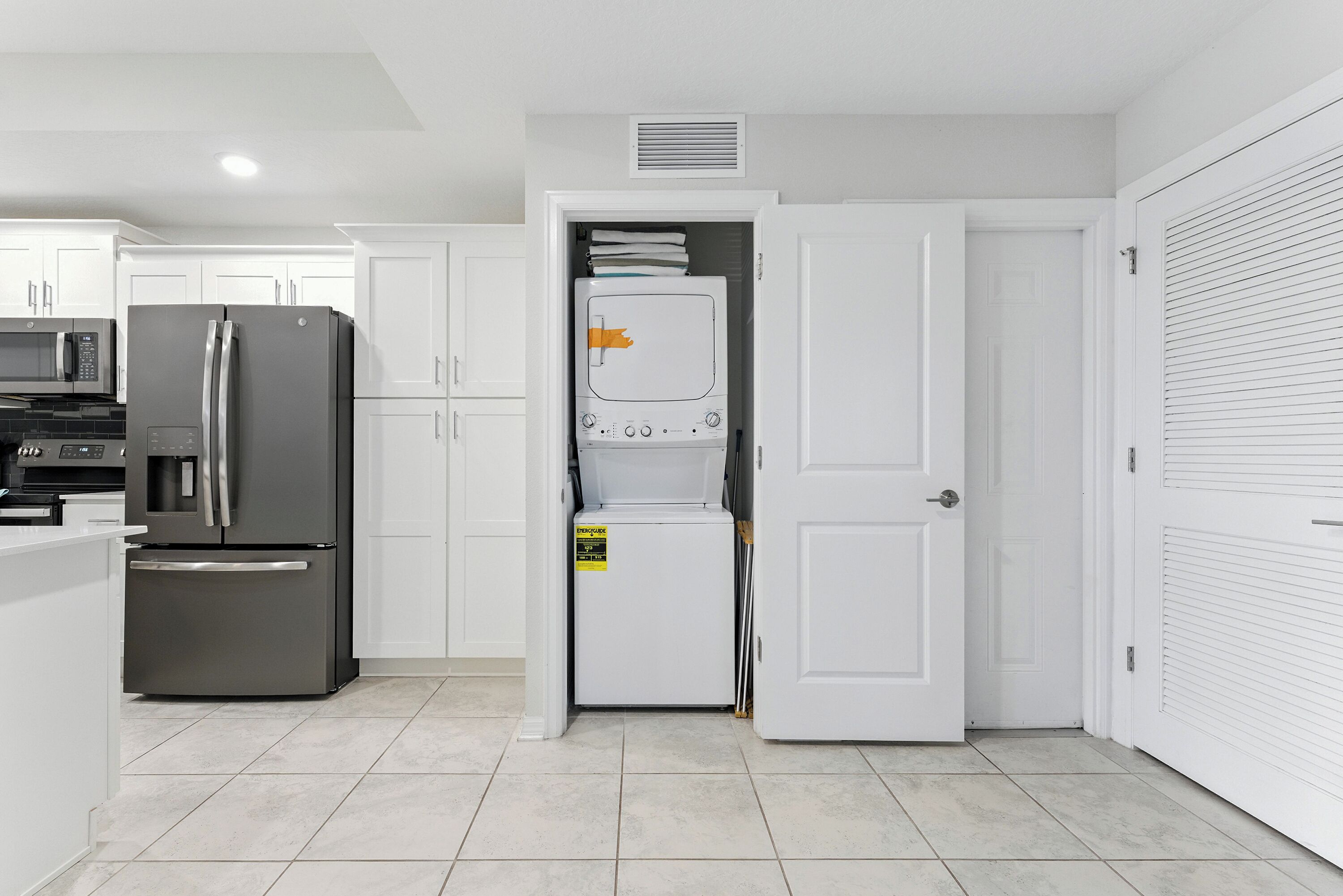 A modern kitchen with white cabinetry, a stainless steel refrigerator, and a microwave.