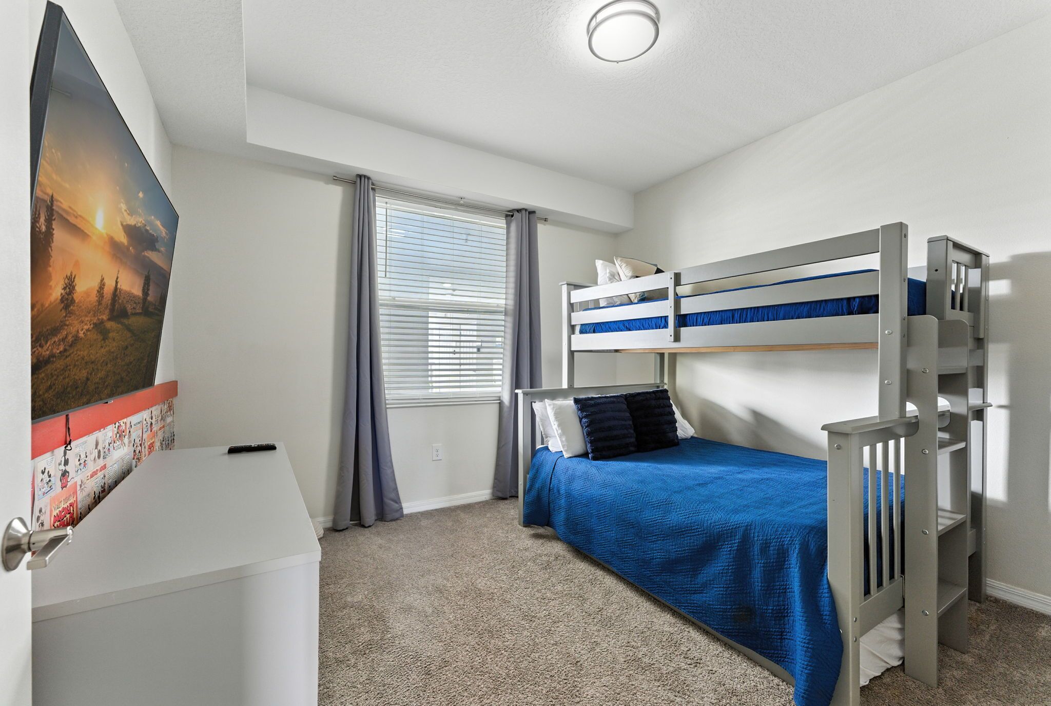 A bedroom with a bunk bed, a desk, a window with curtains, and a poster on the wall.