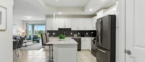 A modern kitchen with white cabinets, a black refrigerator, and a central island with a plant.