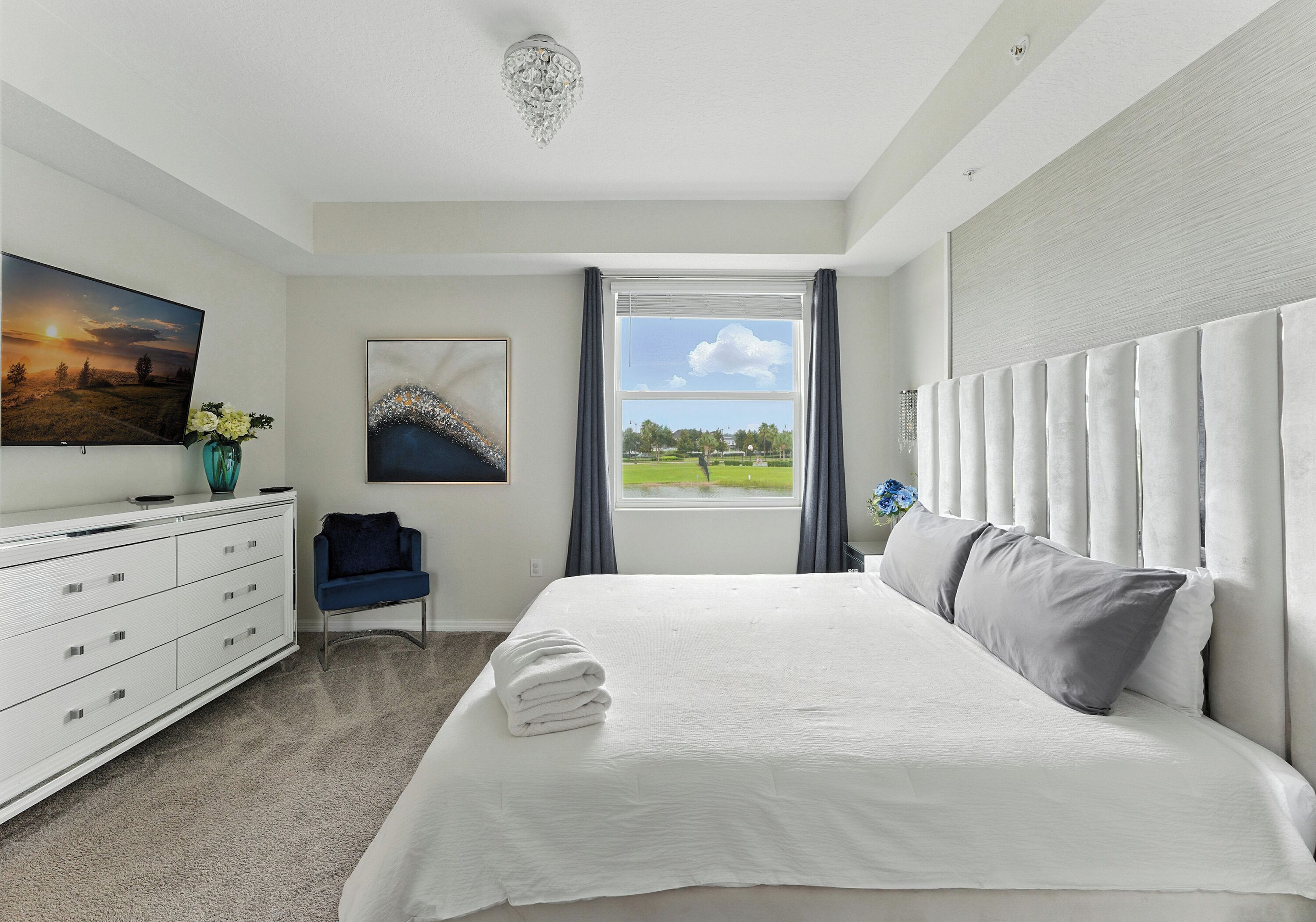 Une chambre avec un grand lit, une commode, une chaise, un téléviseur et une fenêtre donnant sur un parc.
