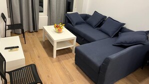 Una sala de estar moderna con un sofá azul oscuro, una mesita de centro blanca con fruta y una silla negra.