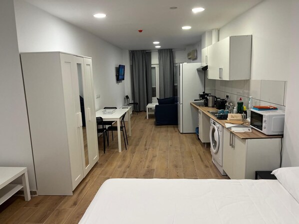 Una habitación de hotel compacta con kitchenette, comedor y cama.