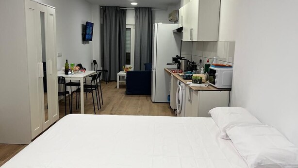 Una habitación de hotel compacta con una cama individual, una kitchenette pequeña, un área de comedor y un baño separado.