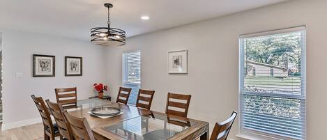 A dining area with a glass-top table, wooden chairs, and a chandelier.