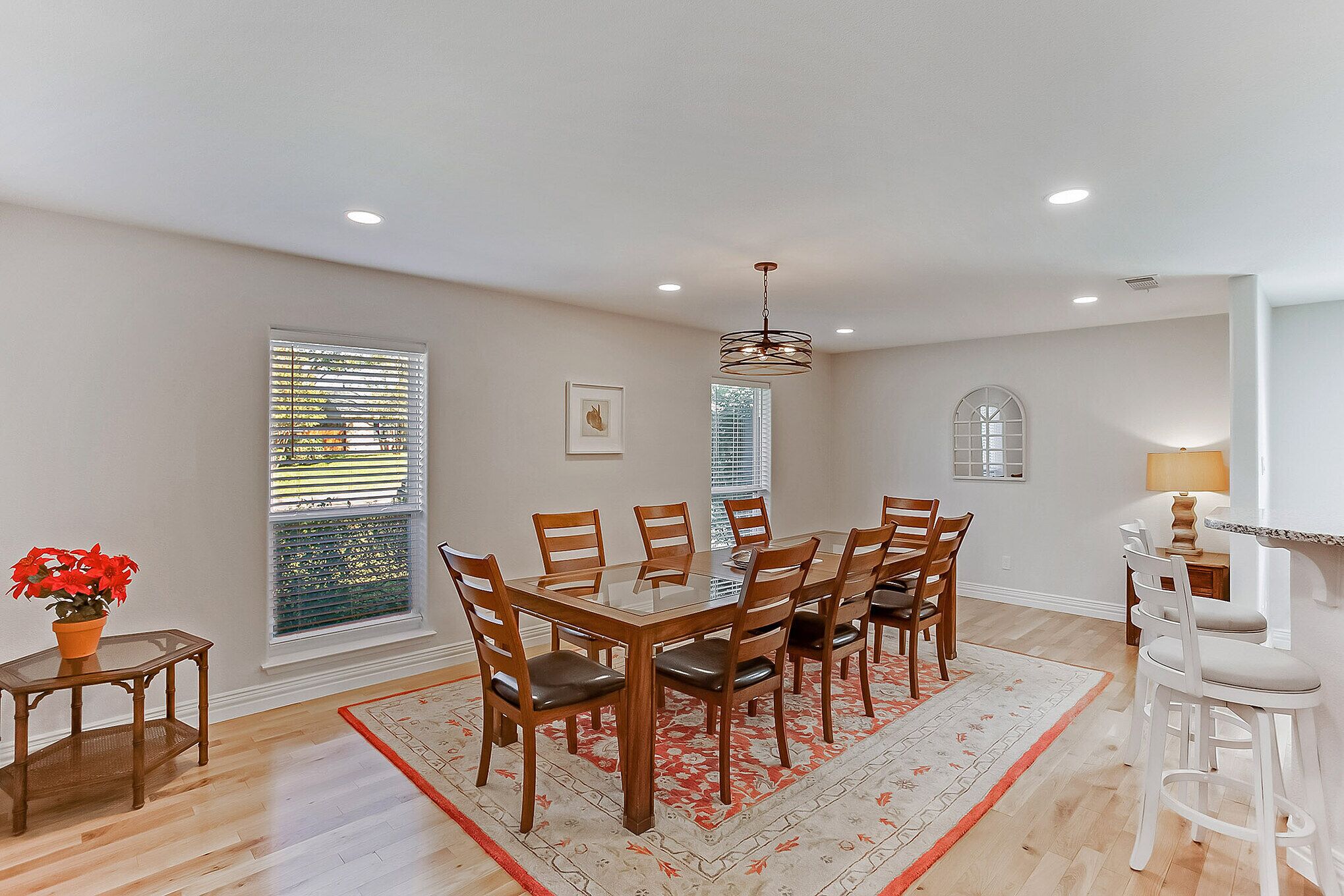 A dining area with a rectangular table surrounded by chairs, a hanging light fixture, and a window with blinds.