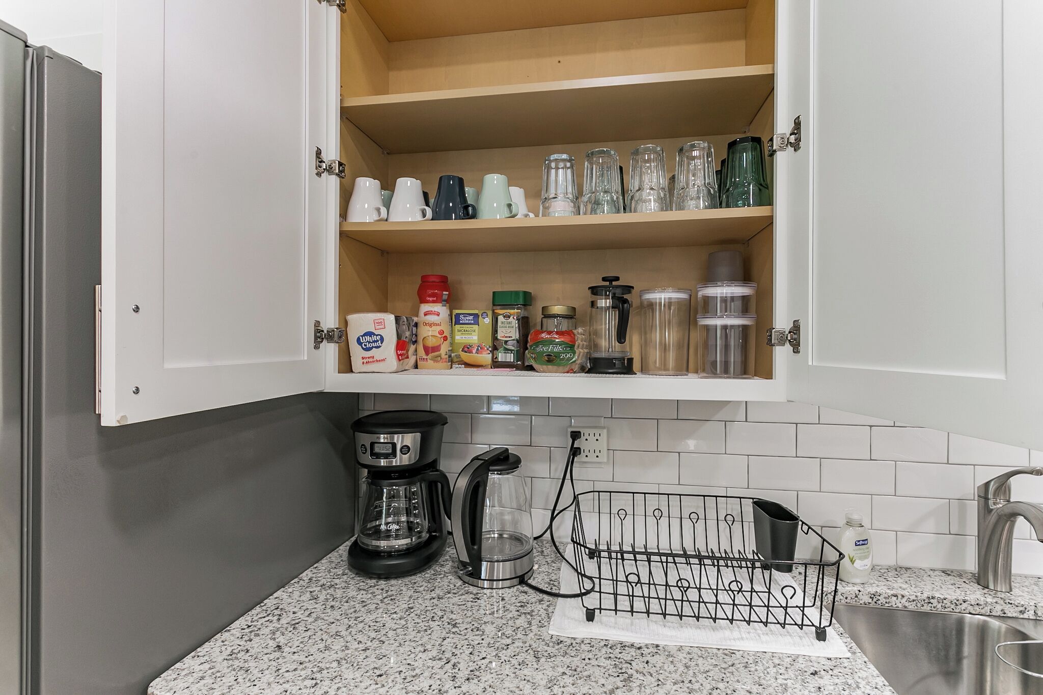 Een keuken met een inbouwkast, koffiezetapparaat, waterkoker en een afwasschaal.