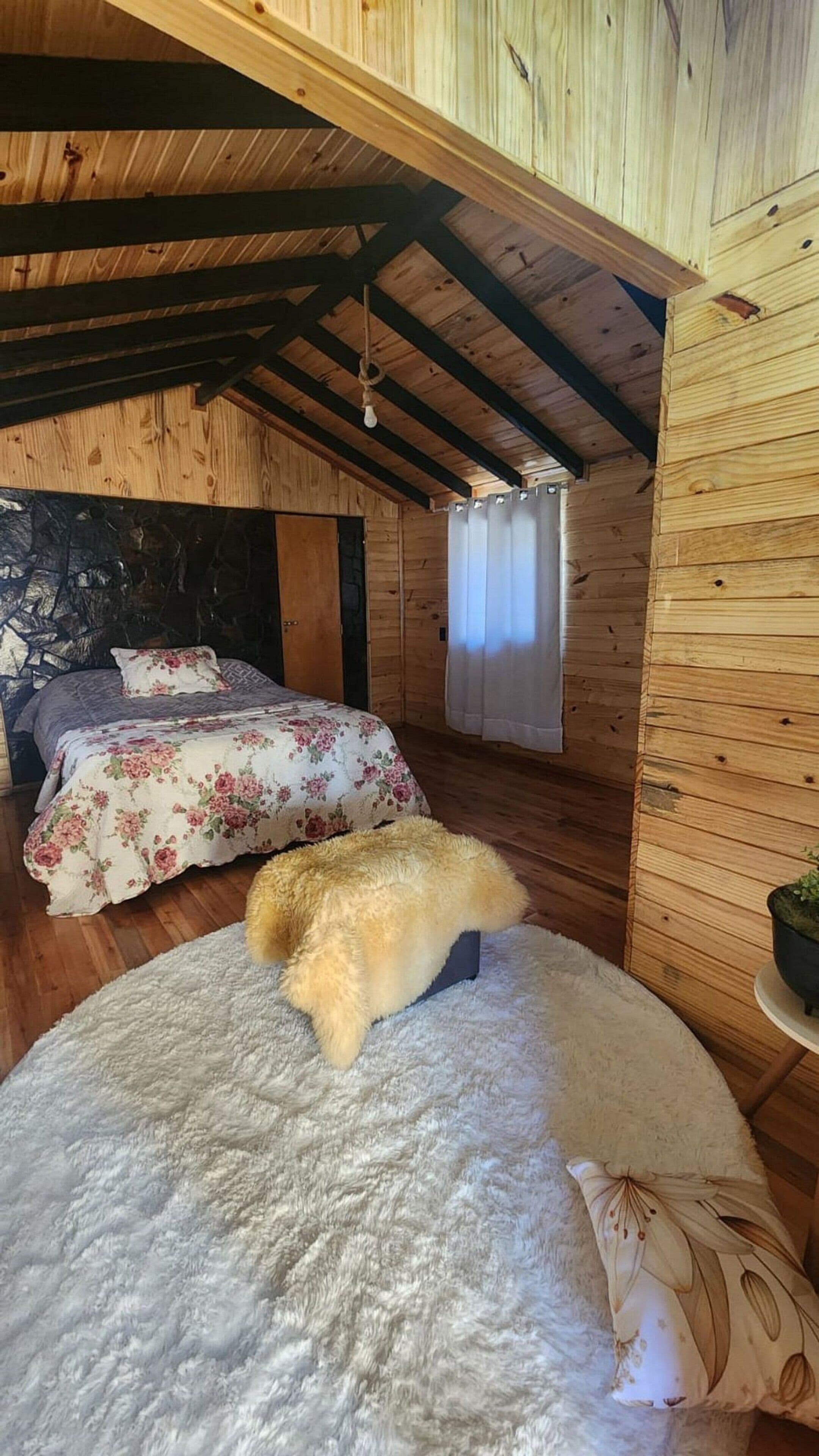 A cozy cabin room with a bed, a fluffy rug, and a wooden ceiling.