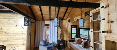 A cozy cabin interior with a wooden ceiling, a sofa, a bed, and a fireplace.