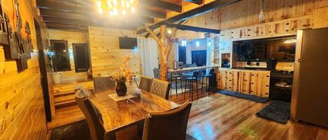 Un interior de madera acogedor con comedor, cocina y un gran tronco de árbol como elemento central.