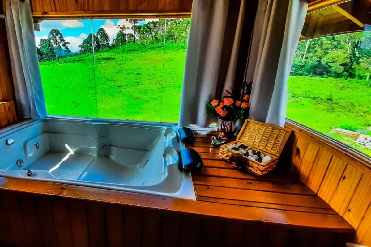 A wooden cabin with a hot tub, a wooden bench, and a view of a green landscape.
