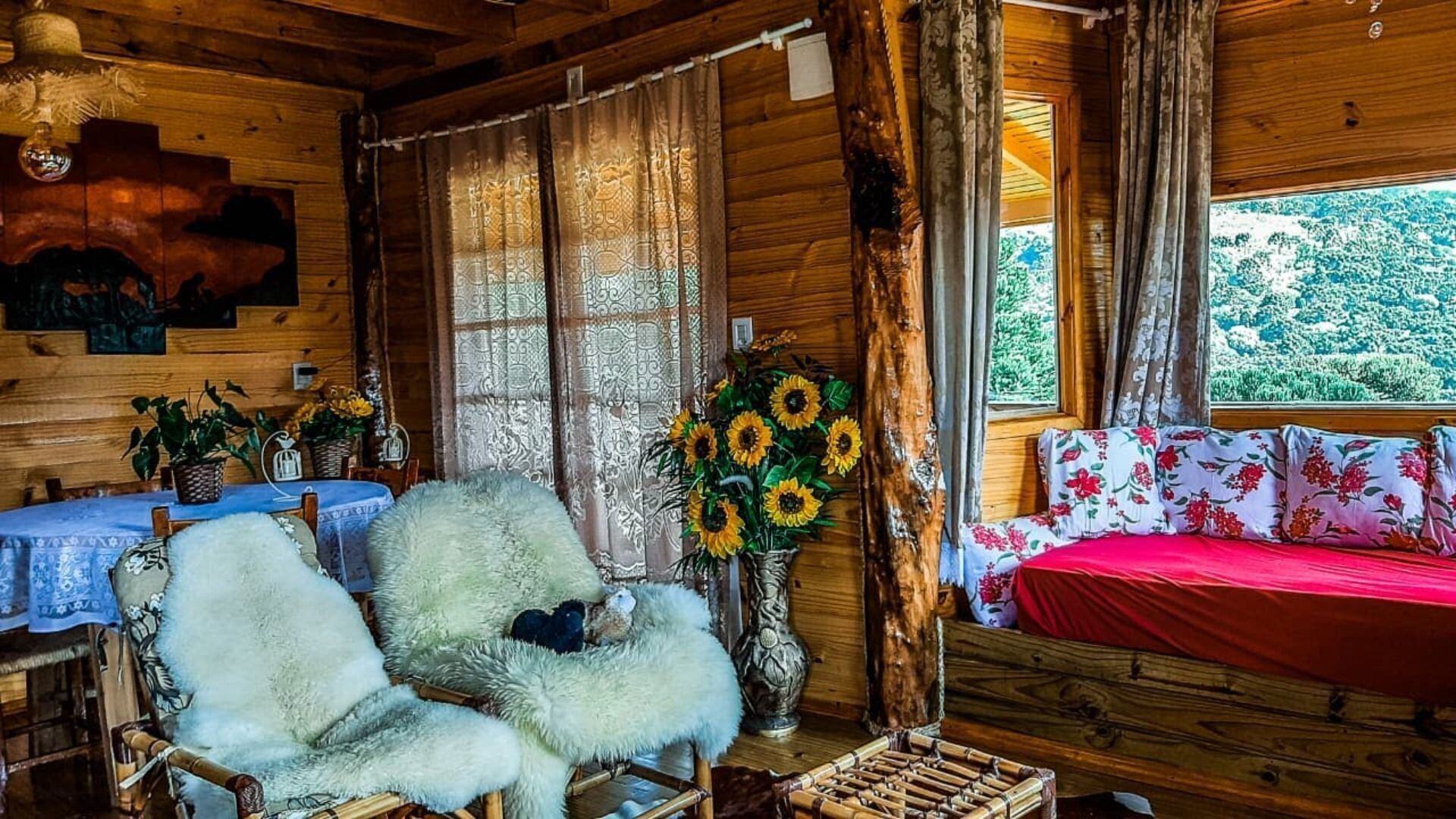 A rustic cabin interior with a wooden interior, a bed with floral bedding, a chair with a fur throw, and a window with a view of greenery.