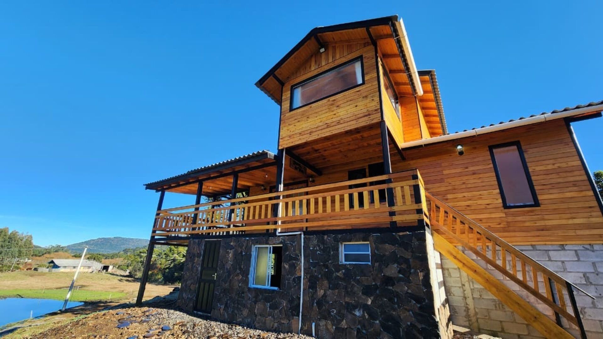 A modern two-story wooden house with a stone foundation, a balcony, and a view of the surrounding landscape.