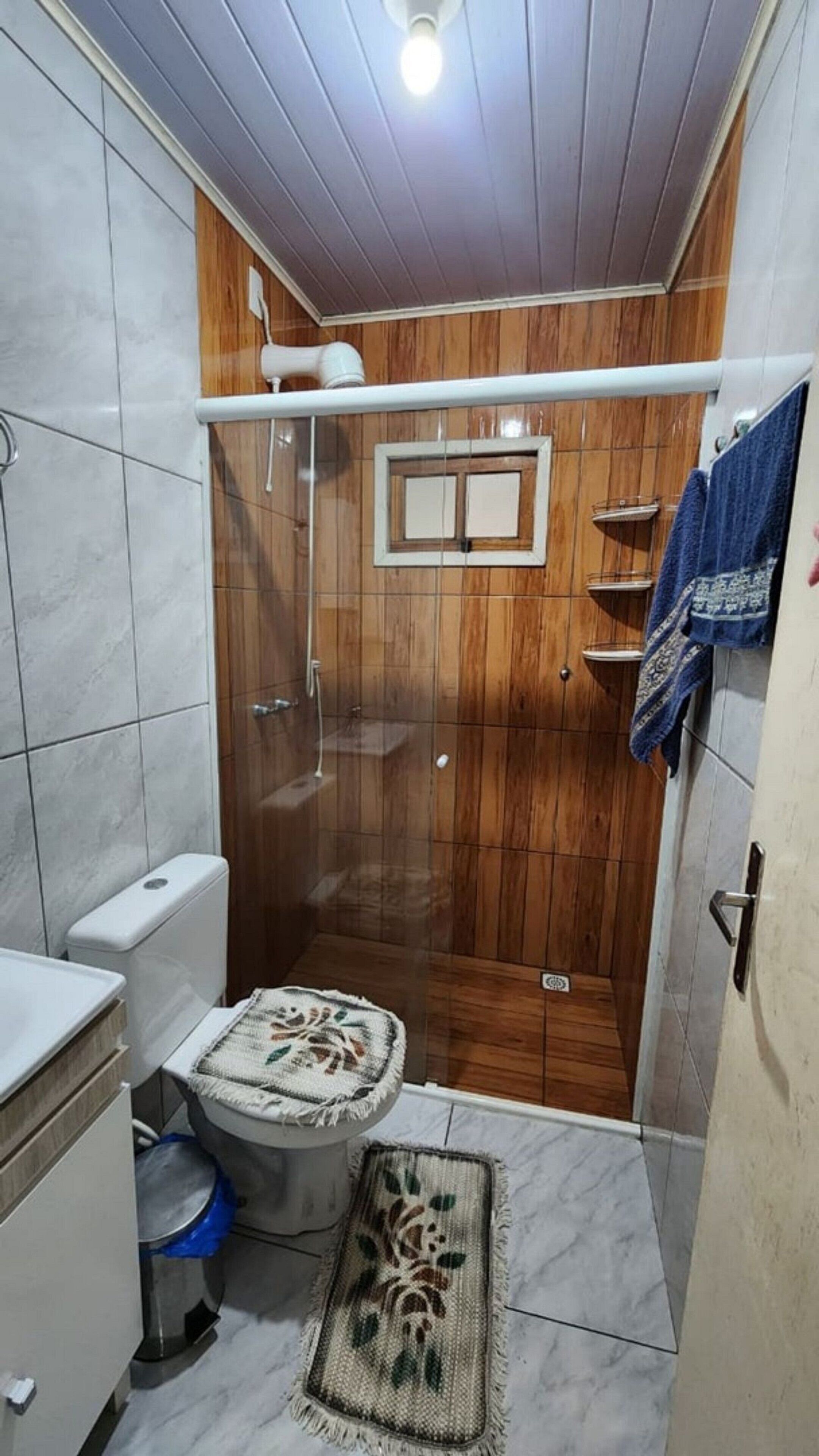 A compact bathroom with a wooden shower enclosure, a toilet, and a small rug on the floor.
