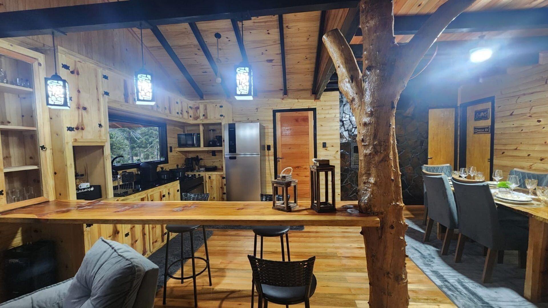 A wooden cabin interior with a kitchen, dining area, and bar.