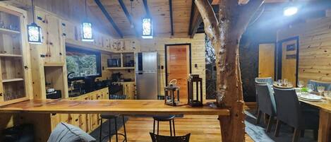 A wooden cabin interior with a kitchen, dining area, and bar.