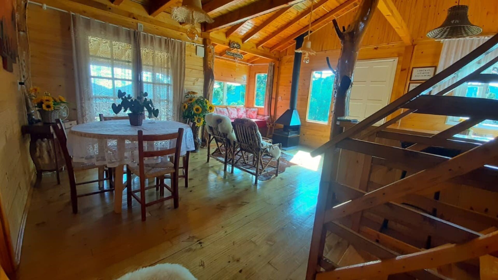 A wooden cabin interior with a dining area, a sofa, and a staircase.