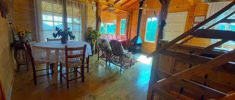 A wooden cabin interior with a dining area, a sofa, and a staircase.