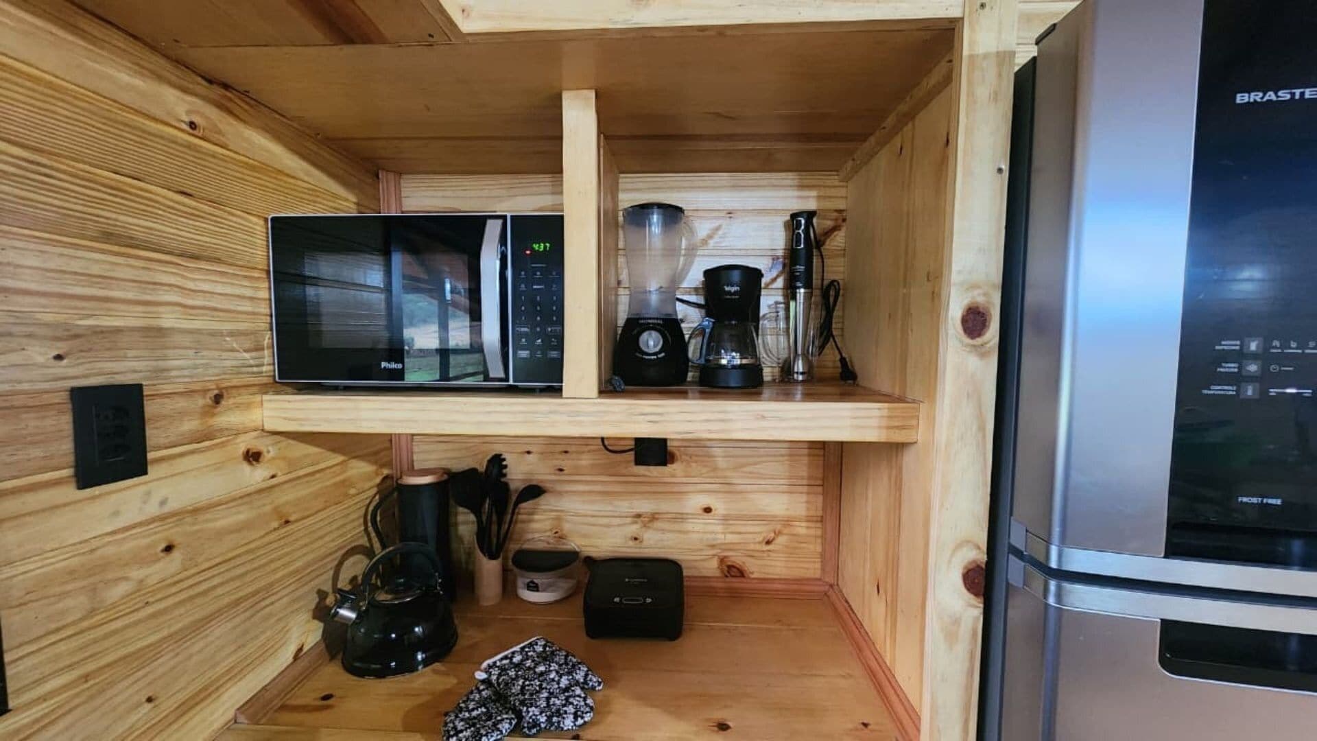 Cocina compacta con microondas, cafetera y hervidor sobre una repisa de madera.